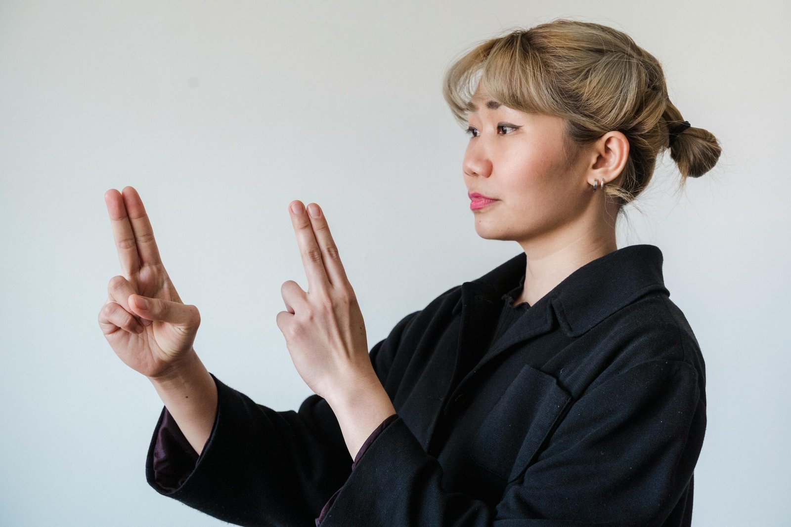 Asian woman gesturing with hands, demonstrating sign language on a white background.